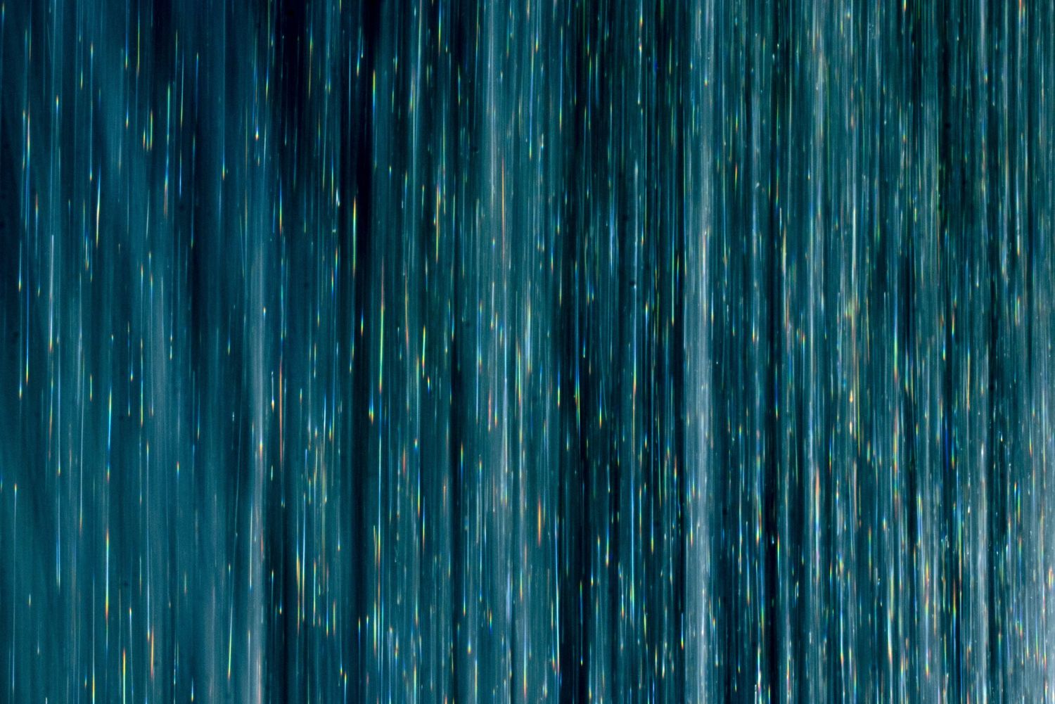 Abstract blue and teal streaks of falling rain creating a textured pattern background.