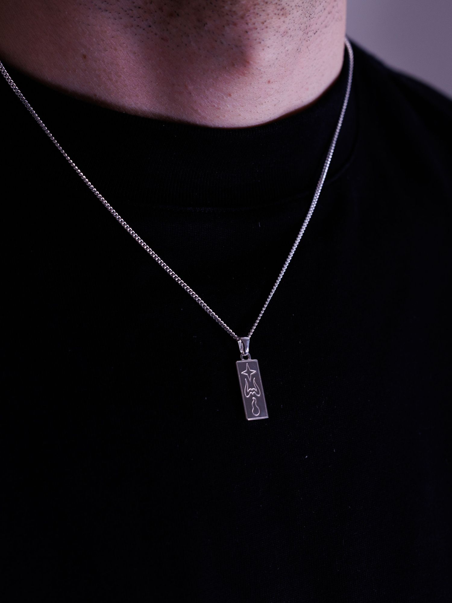 Man wearing black t-shirt with silver chain necklace featuring a rectangular bar pendant with star design.