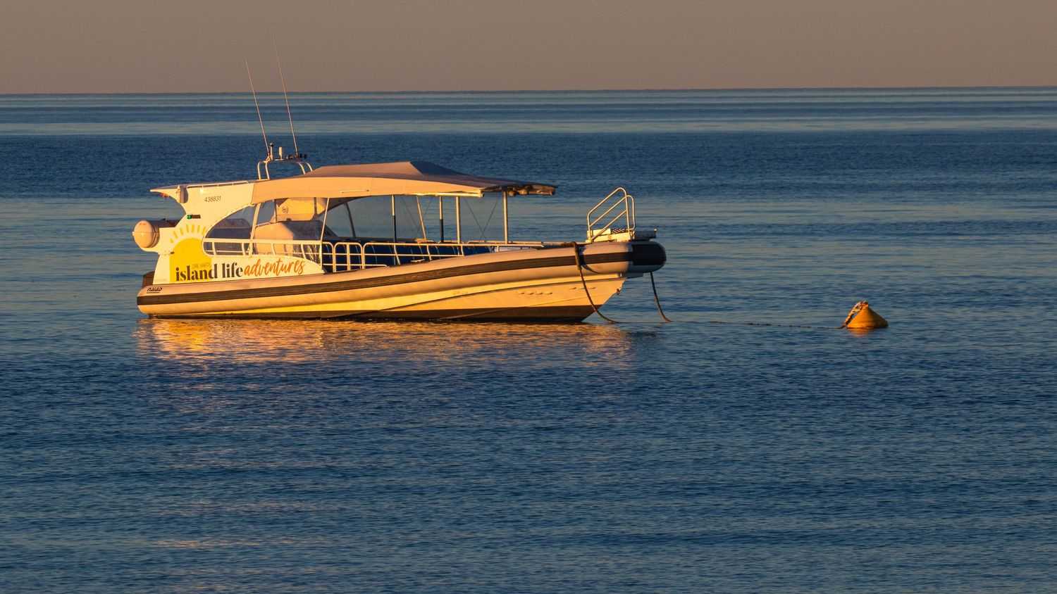 Yellow and white motorboat moored on calm glassy ocean at golden sunset with buoy marker nearby.