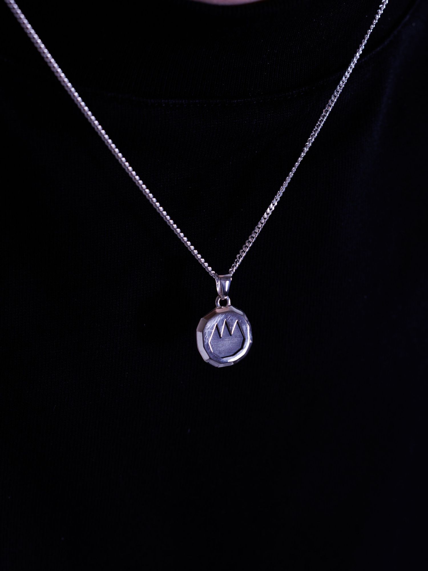 Person wearing silver round crown engraved pendant on box chain necklace.