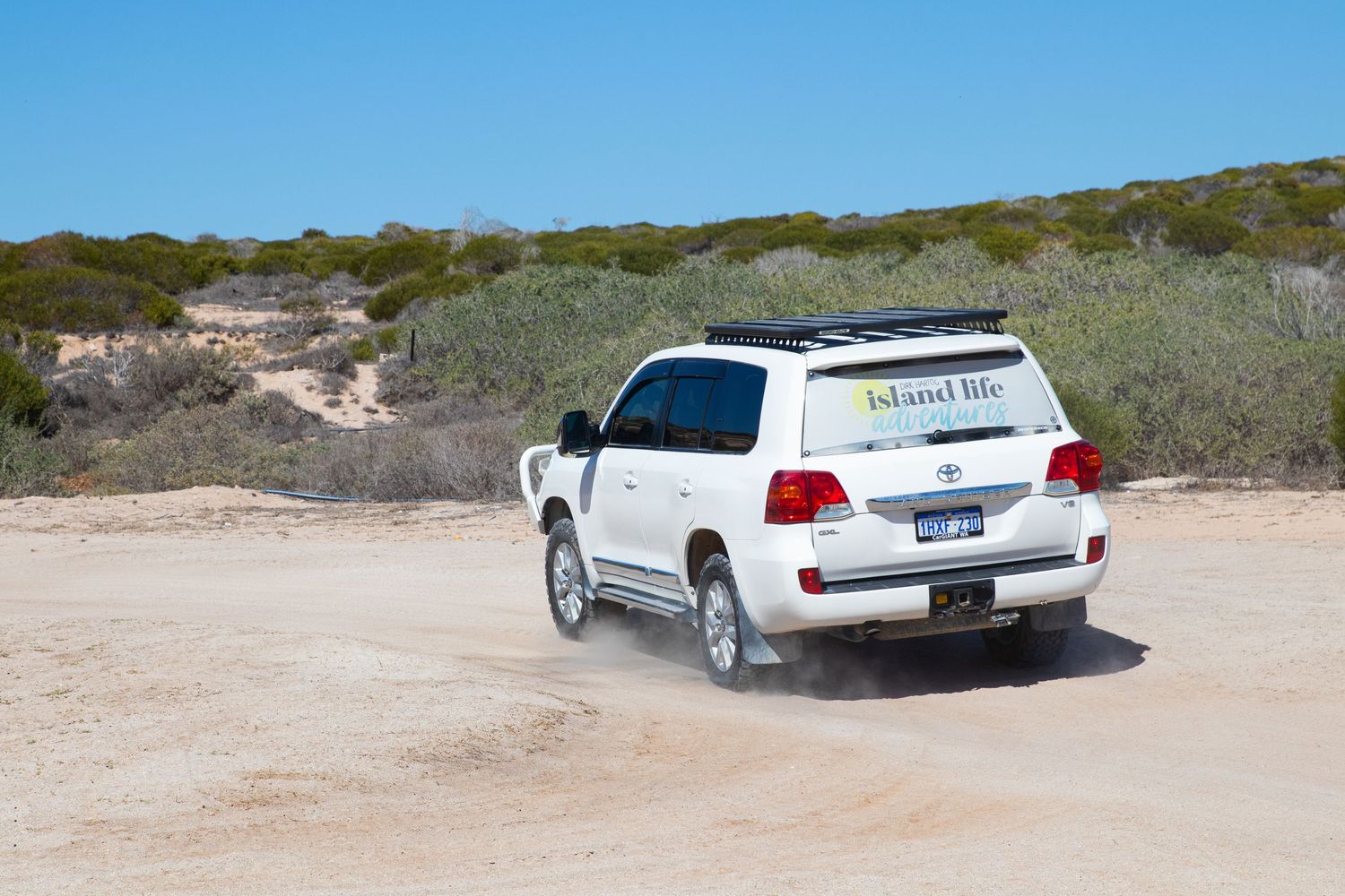 White Island Life Tours Toyota Land Cruiser driving along sandy remote outback track with coastal scrub vegetation.