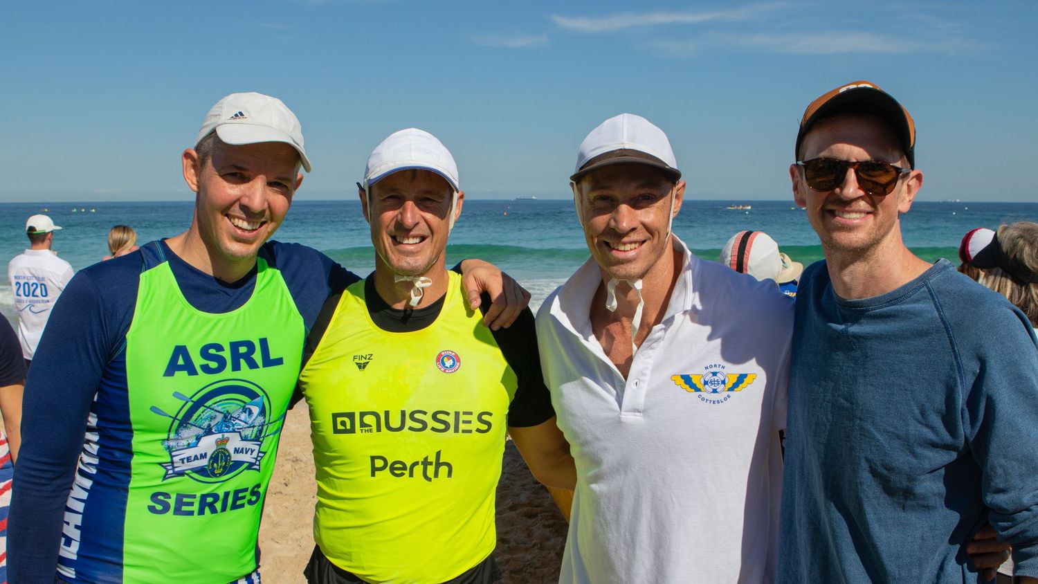 Four men pose together on a sunny beach during an ASRL surf boat rowing series event in Perth.