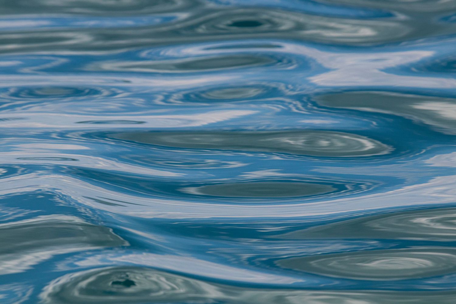 Smooth blue water surface with gentle swirling ripples creating an abstract pattern.