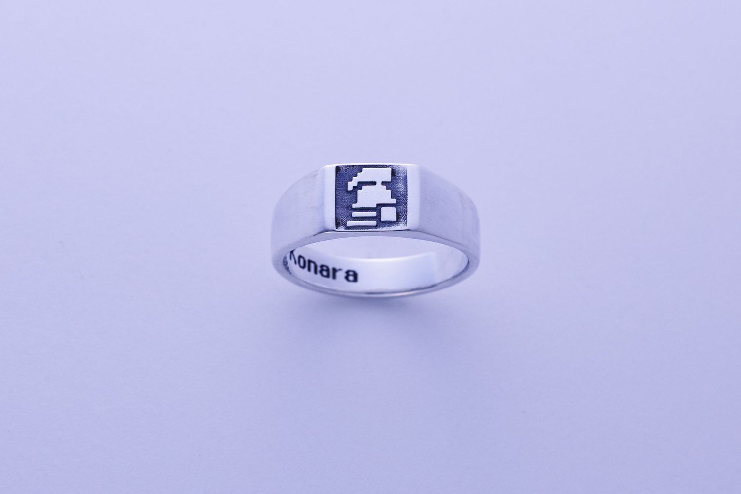 Silver ring with pixel art video game character design on flat top surface with engraved text on band.