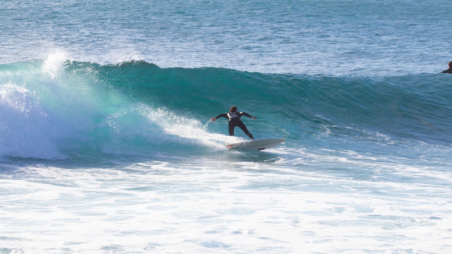 A surfer in a wetsuit rides the face of a turquoise wave at a reef break.