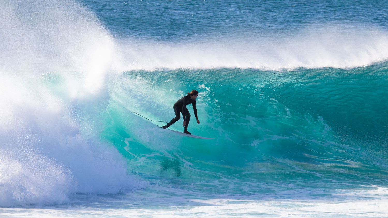 Surfer in black wetsuit performing aerial maneuver on a large crashing turquoise wave.