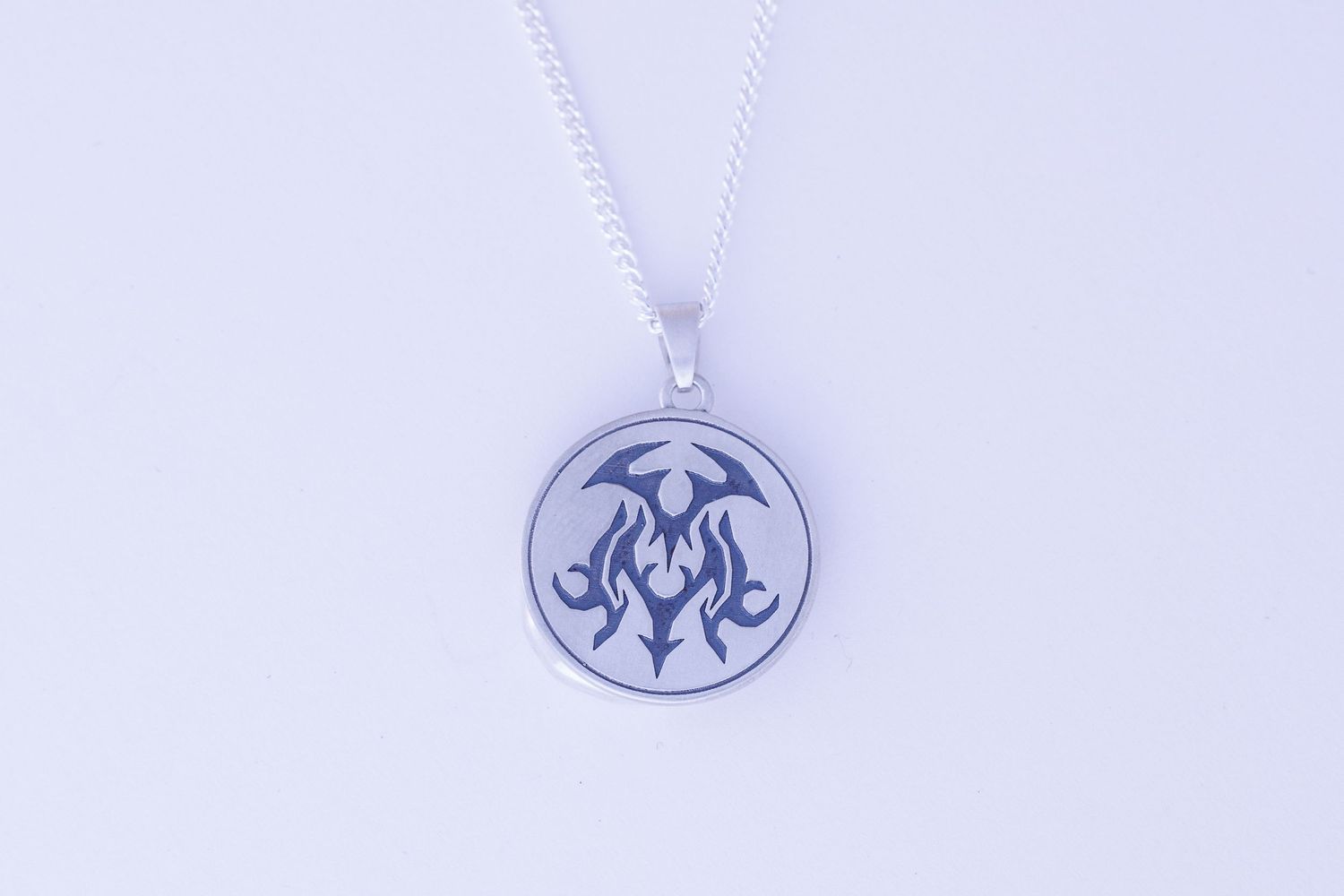 Round silver pendant necklace featuring engraved tribal dragon design on chain.