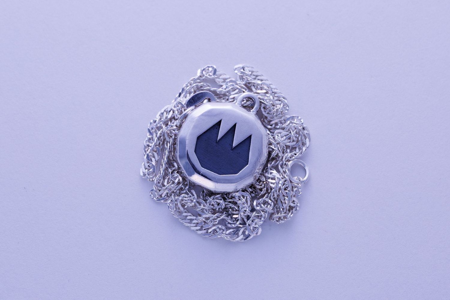Round silver pendant necklace with engraved crown logo design on delicate chain.
