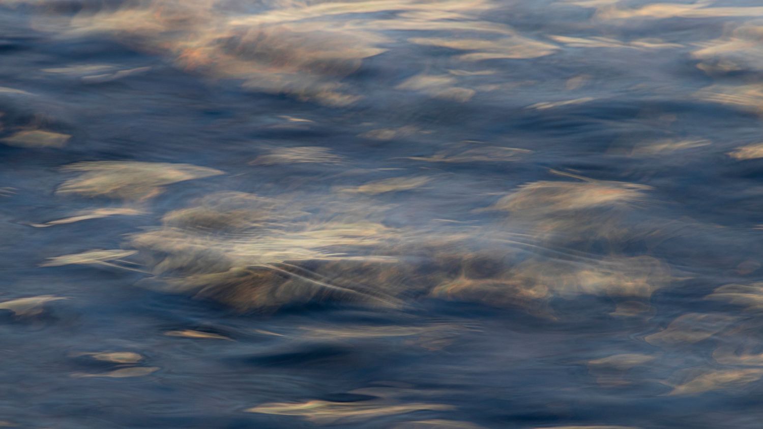 Abstract blue water surface with soft golden reflections creating a painterly texture.
