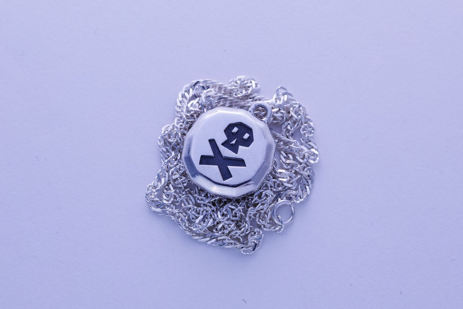 Round silver pendant necklace featuring engraved skull and crossbones design on delicate chain.