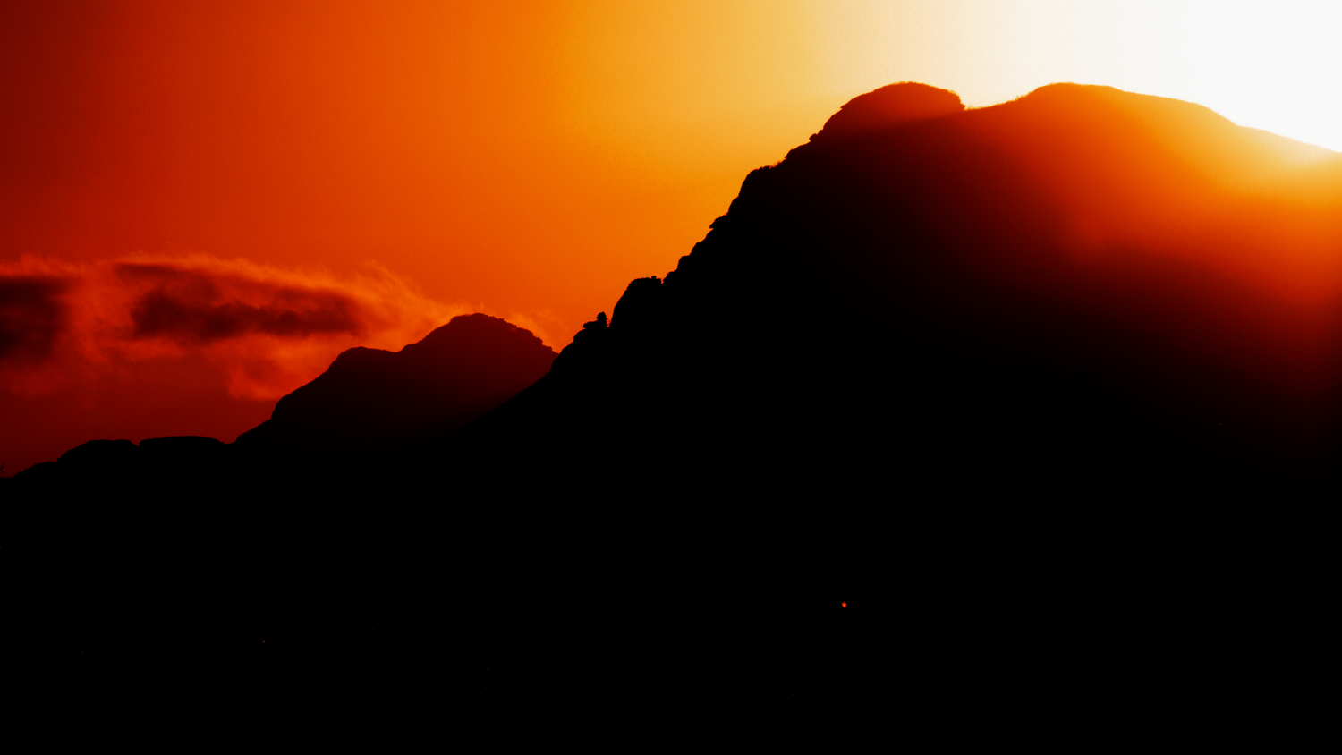 Dramatic silhouette of rugged mountain peaks against a vivid fiery orange sunset sky.