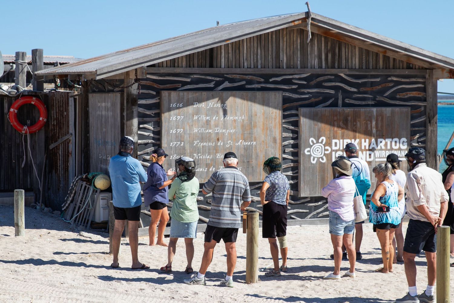 Visitors gathered outside Dirk Hartog Island Outstation heritage building on a sunny beach day.