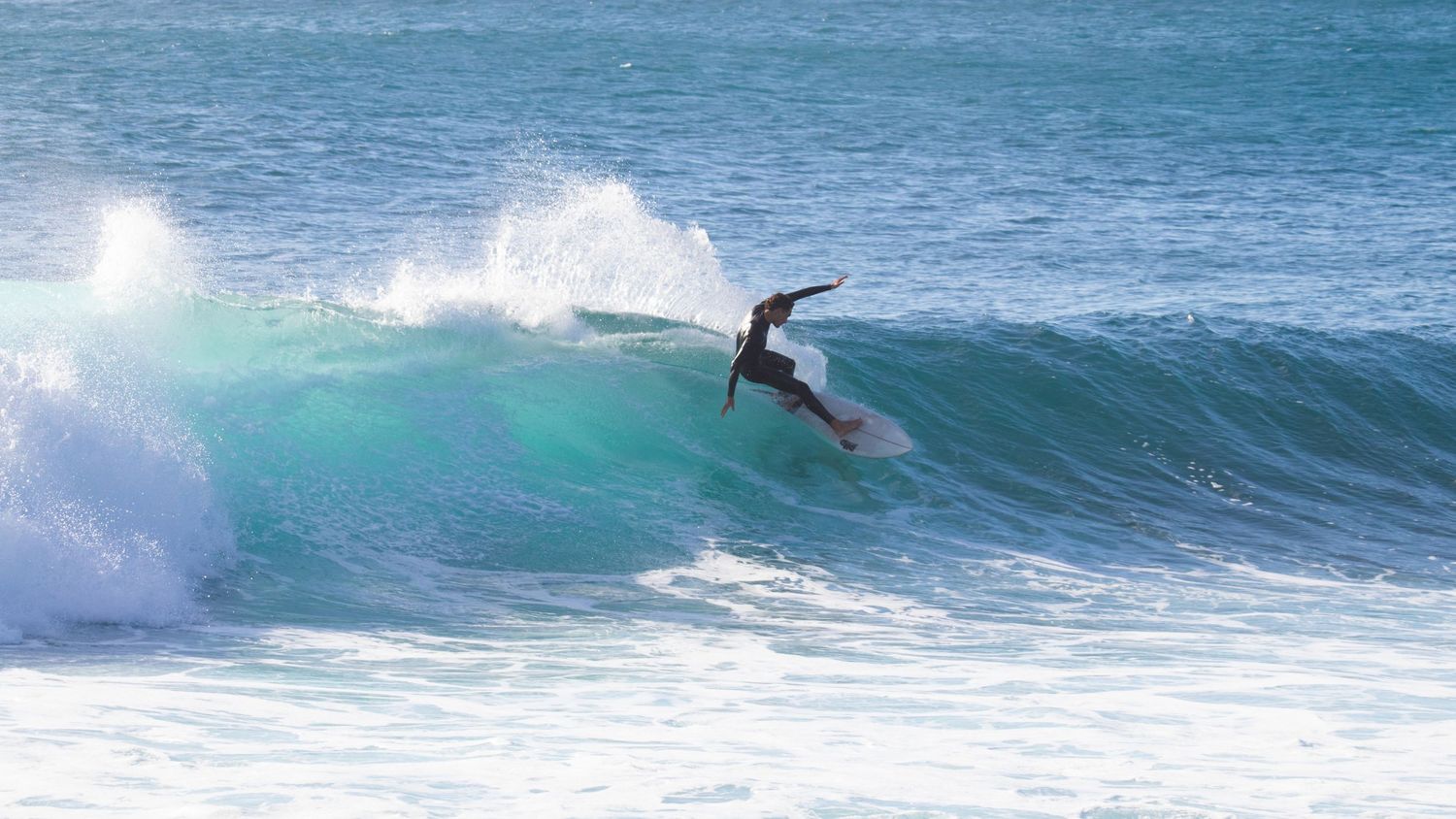 Surfer carving a turn on a stunning turquoise wave at a sunny beach break.