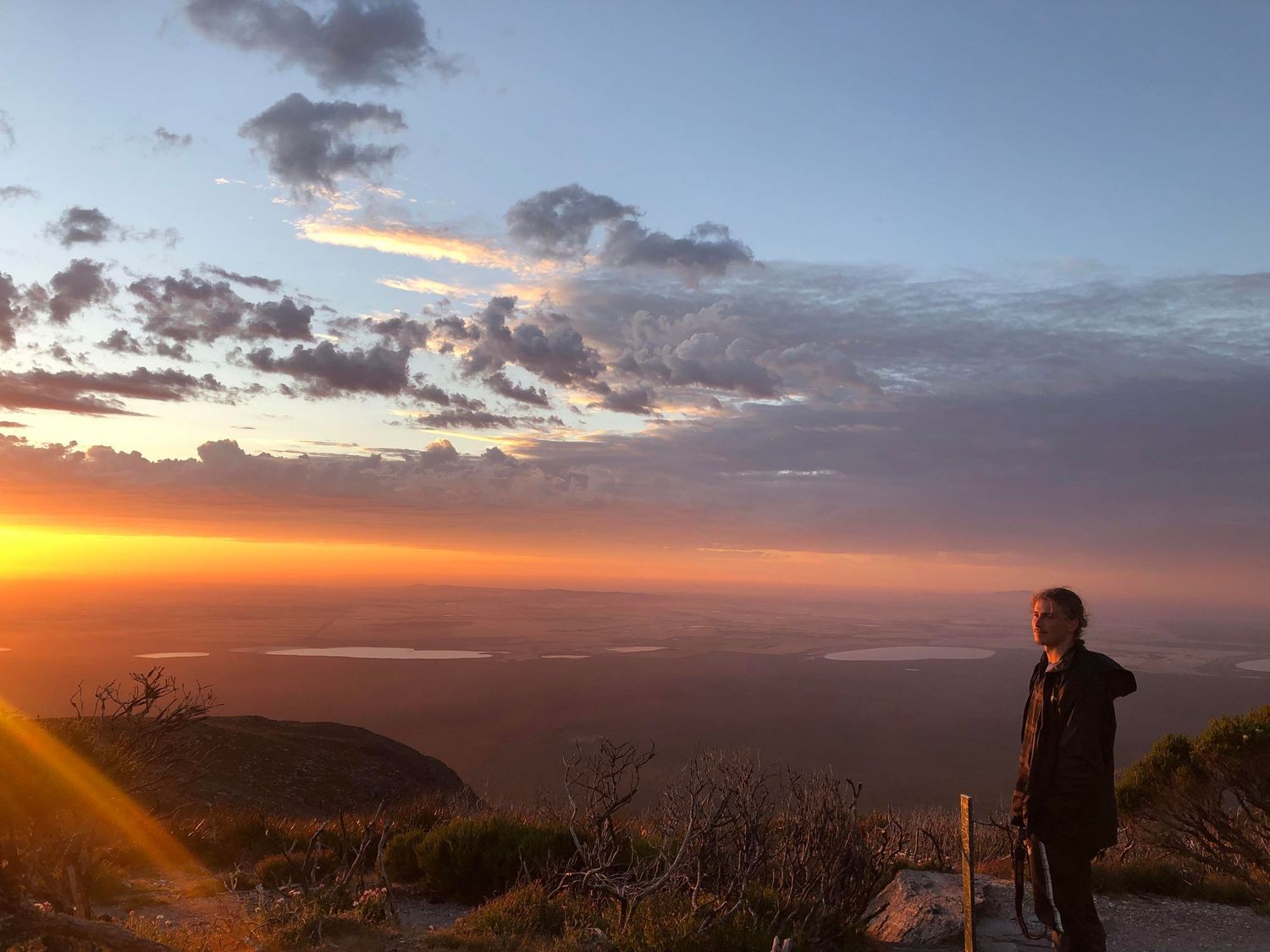 Solo hiker gazing at a breathtaking fiery orange sunset from a scenic mountain overlook.