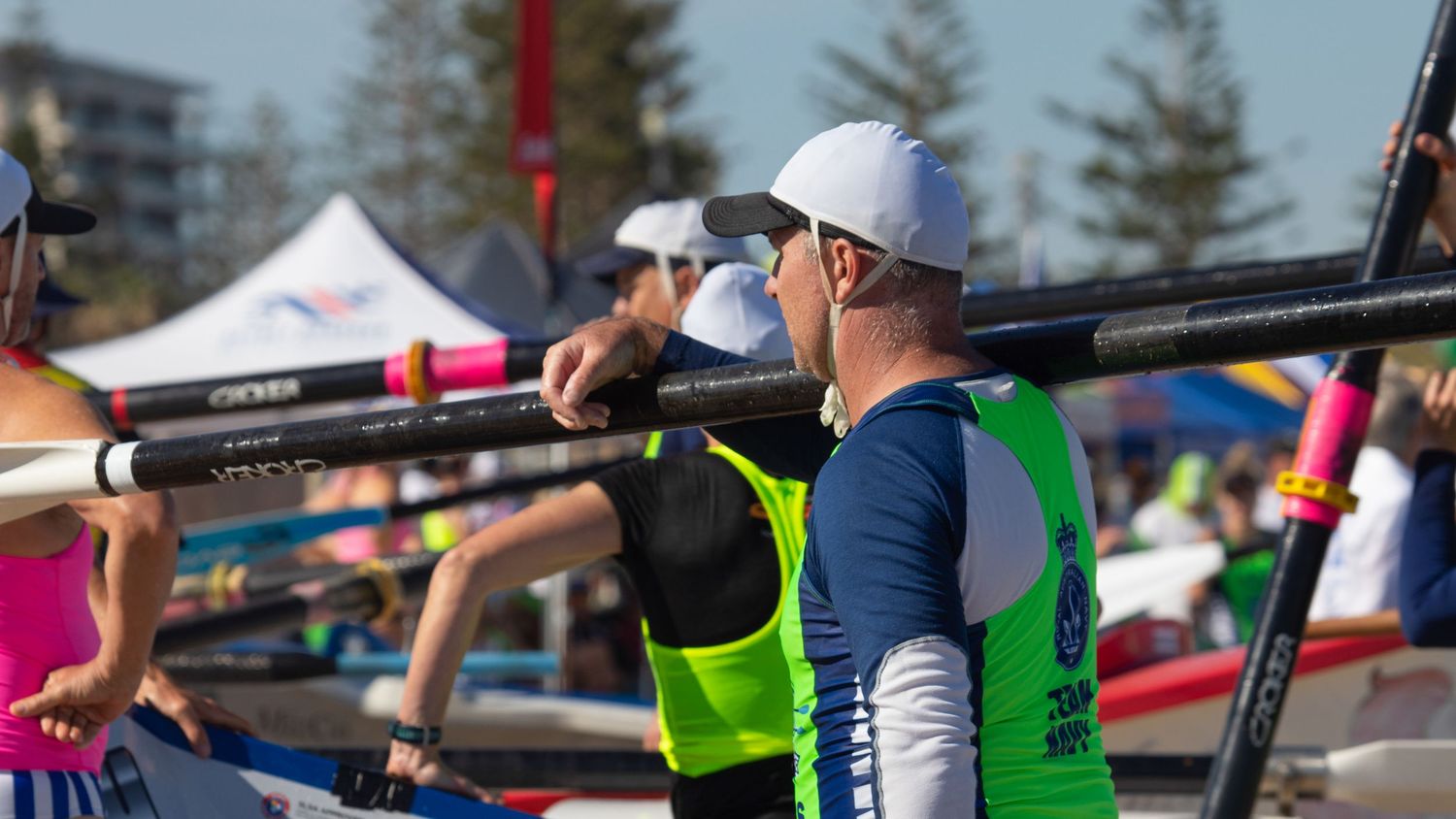 A surf boat rower carries an oar over his shoulder at a busy Australian beach lifesaving carnival.