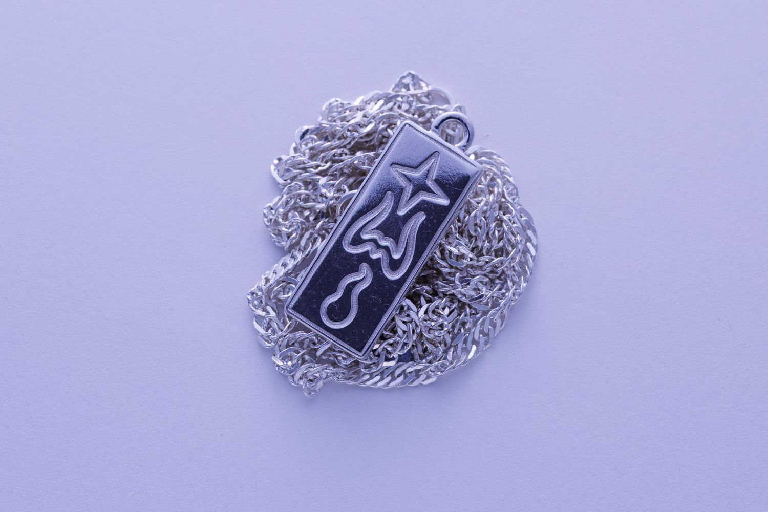 Rectangular silver pendant necklace with engraved star and flame design on twisted rope chain.