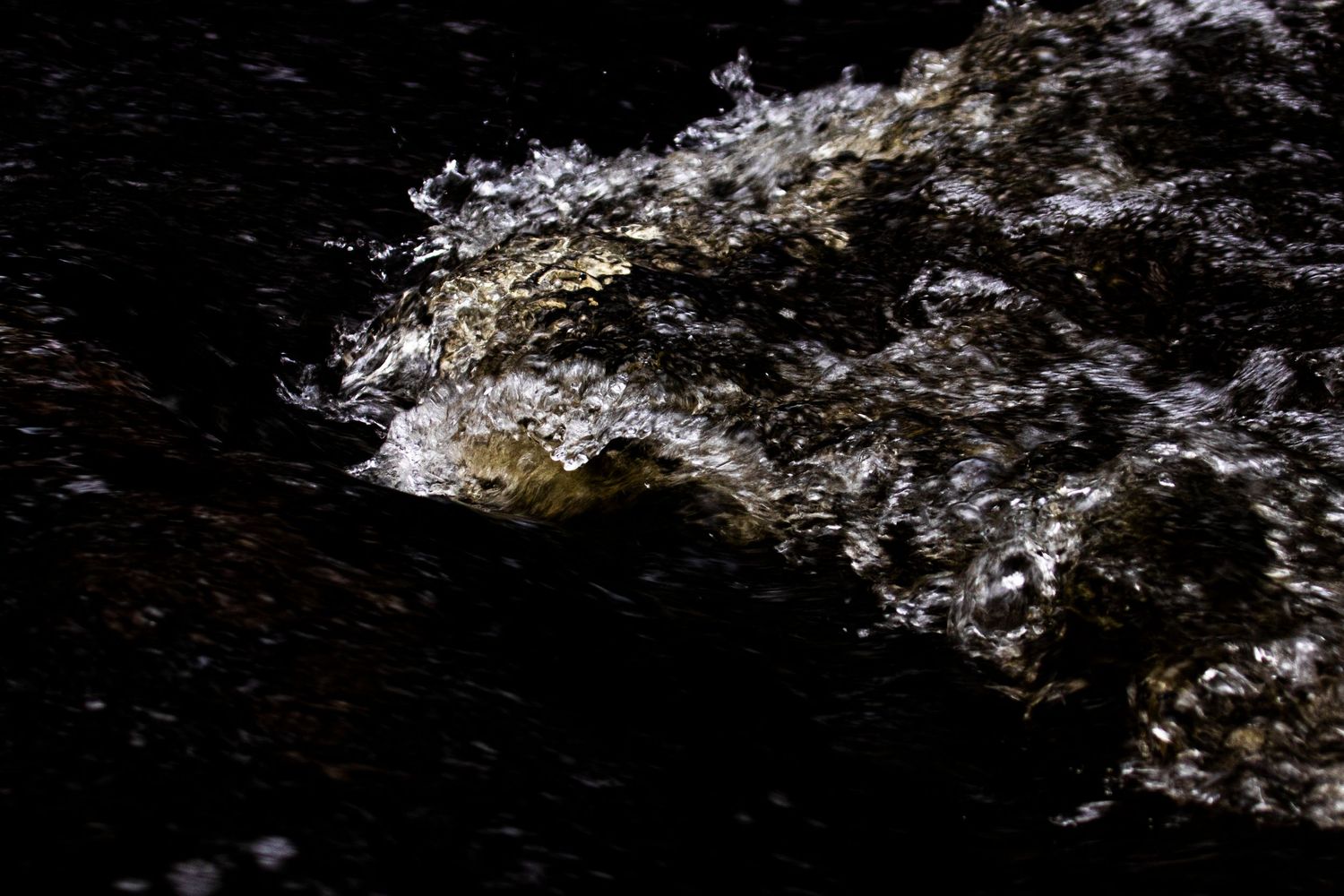 Close-up of dark churning ocean water with white foam and golden light on the surface.