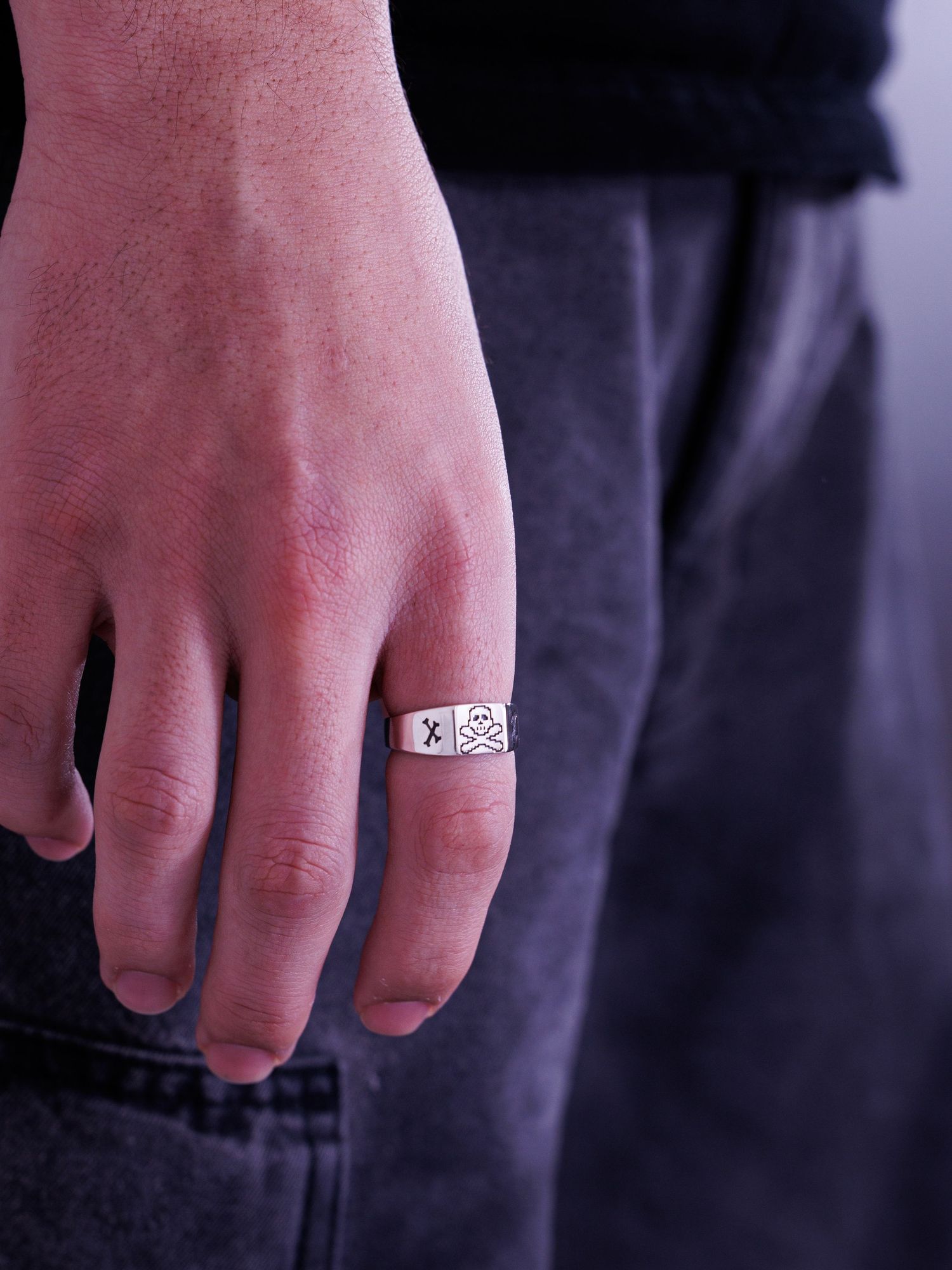 Man's hand wearing a wide silver signet ring engraved with skull and crossbones motif.