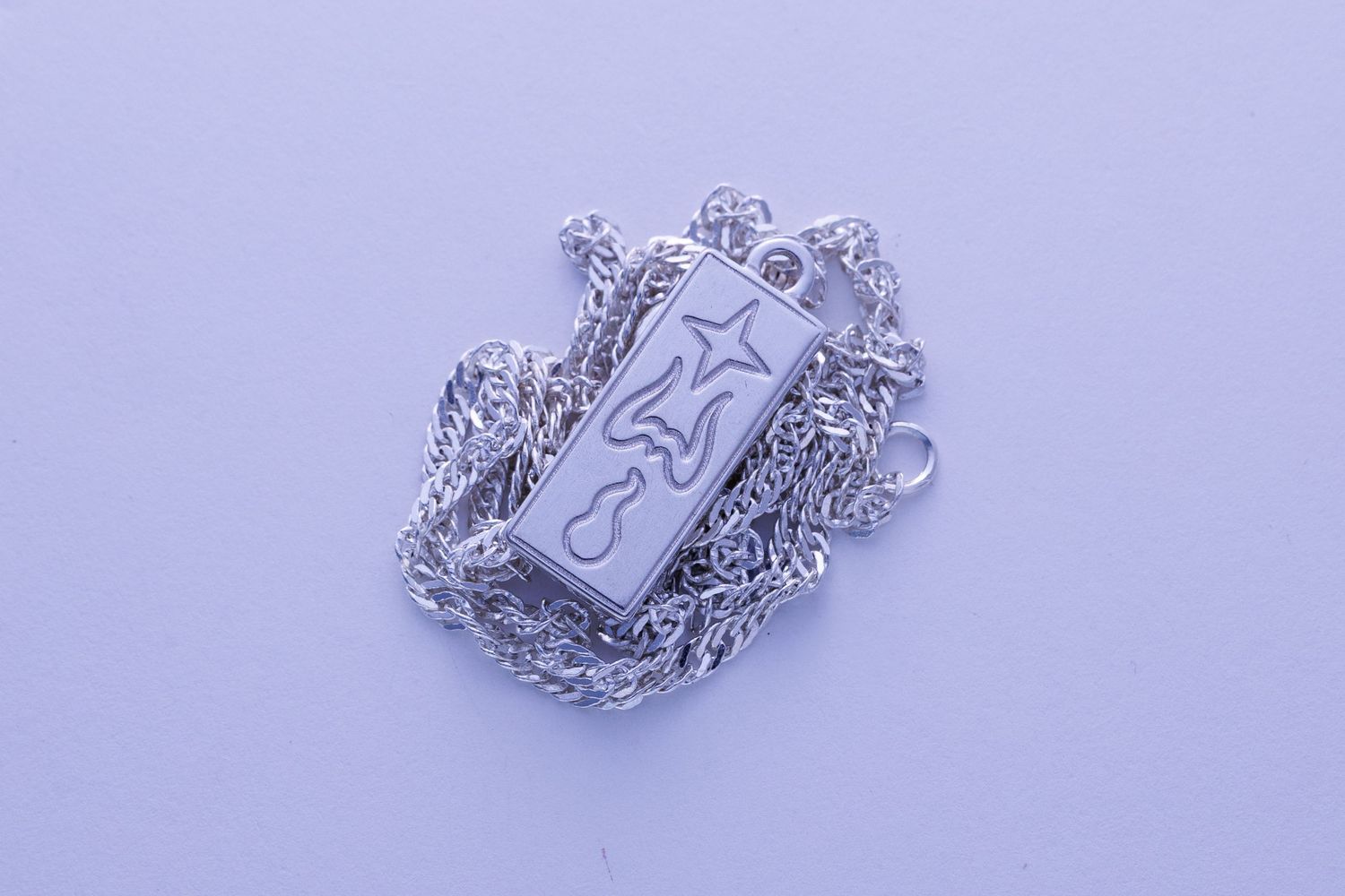 Rectangular silver pendant necklace with engraved star and flame motif on twisted rope chain.
