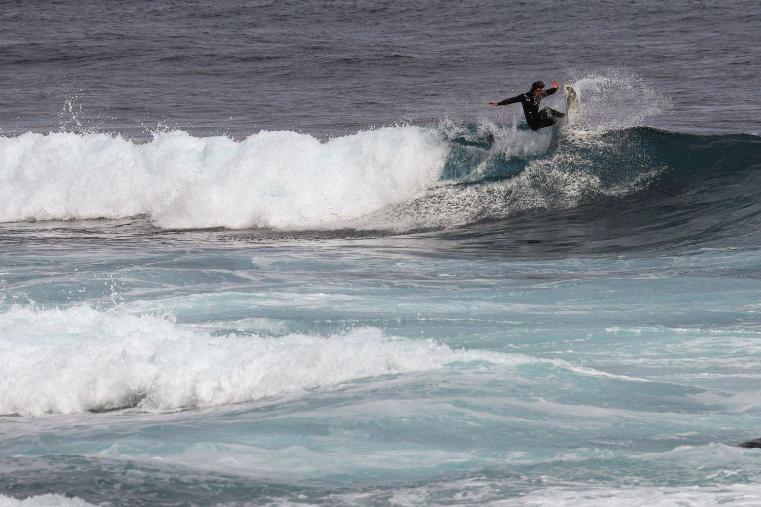 Surfer performing a maneuver on a breaking wave in choppy ocean waters.