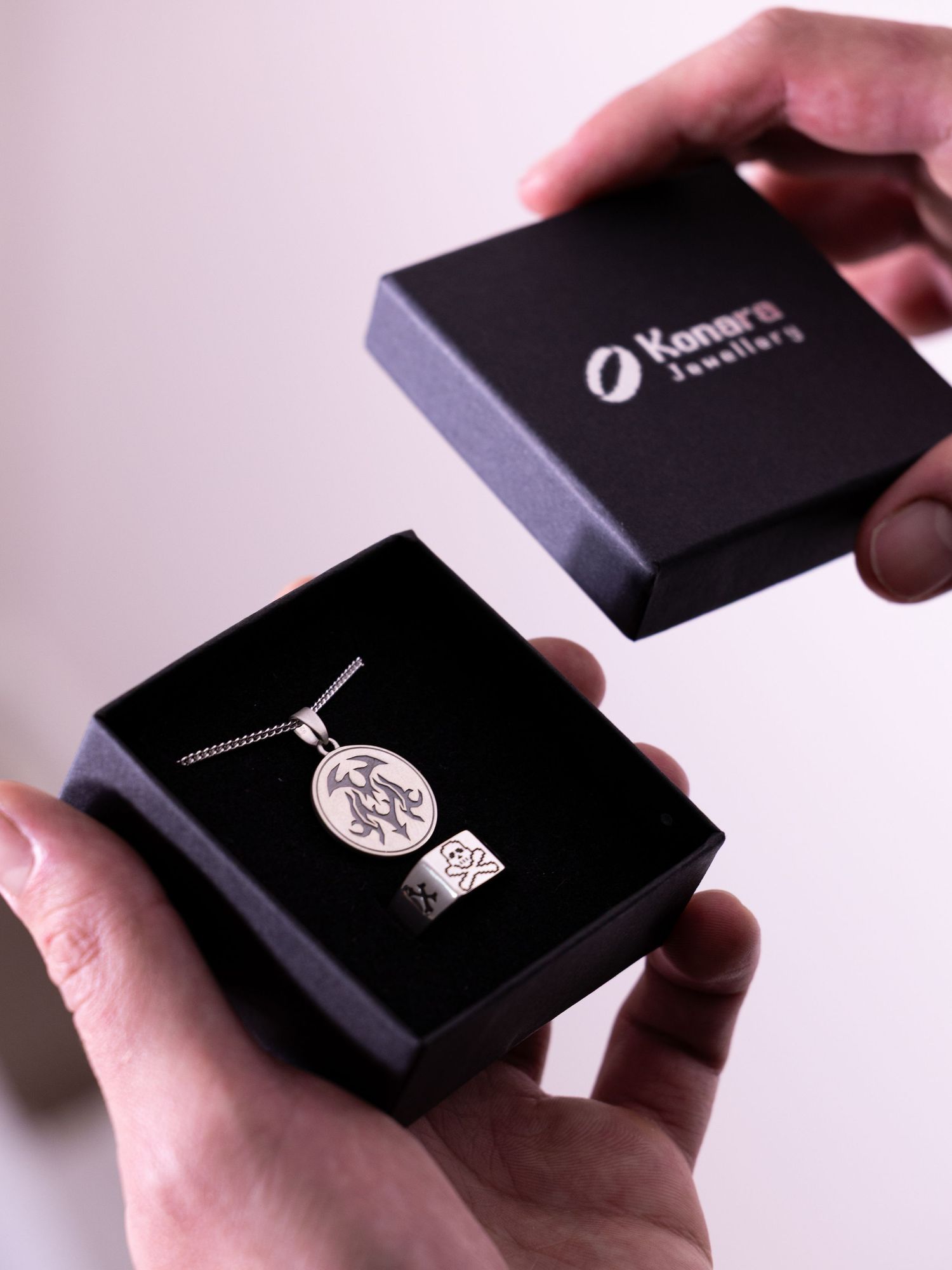 Hands opening a Konara Jewellery black gift box containing a silver pendant necklace and ring.