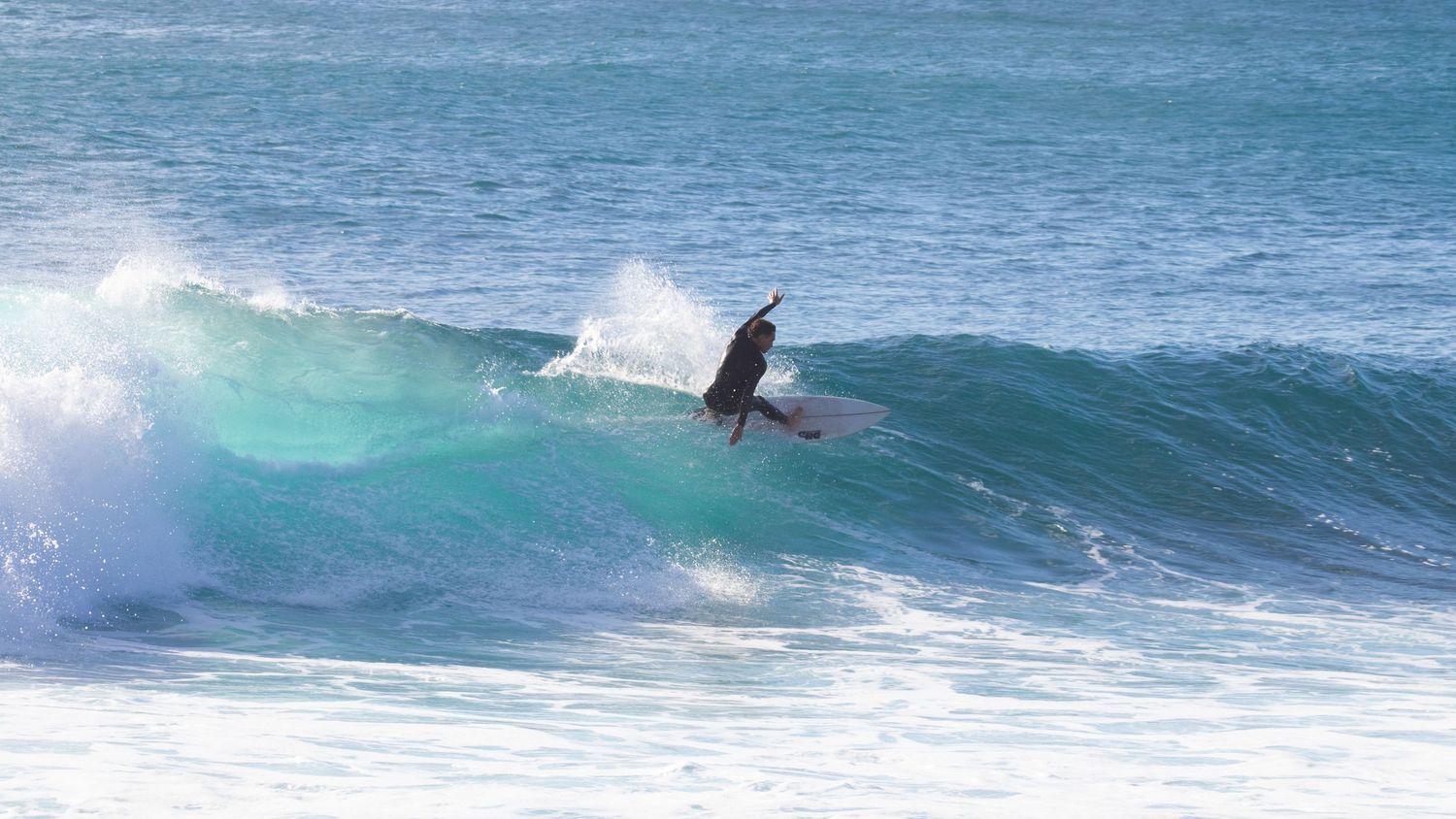 A surfer performs an aerial maneuver above a breaking turquoise ocean wave.