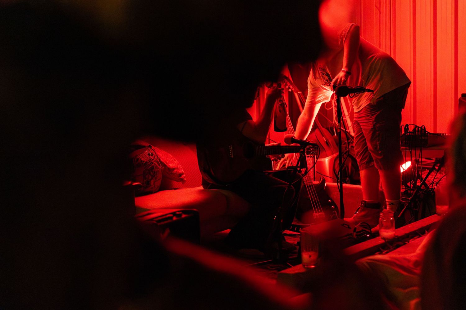 Musicians performing on stage under dramatic red lighting in a dimly lit venue.