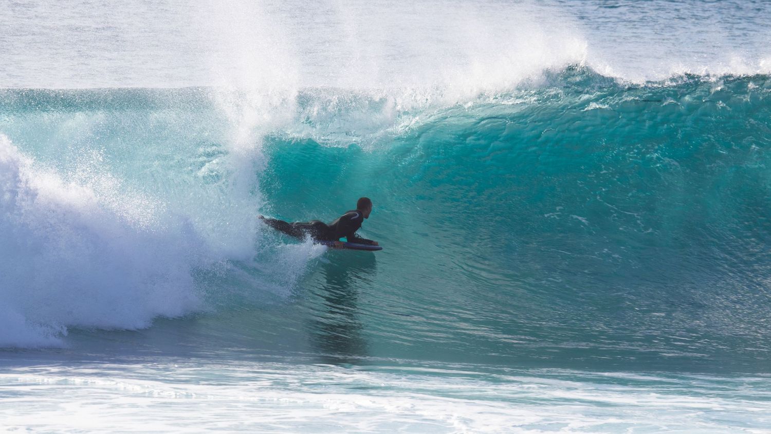 A surfer rides inside a massive turquoise barrel wave at a tropical beach break.
