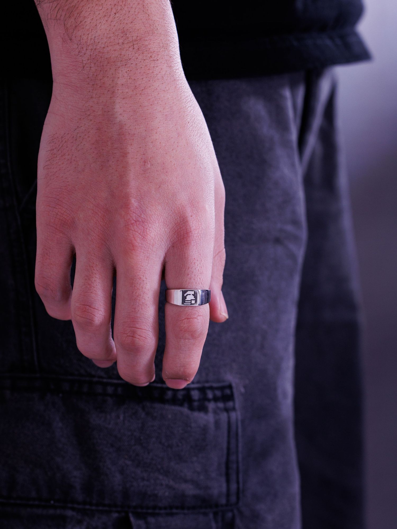 Man wearing a wide silver signet ring with a bold engraved initial on index finger.