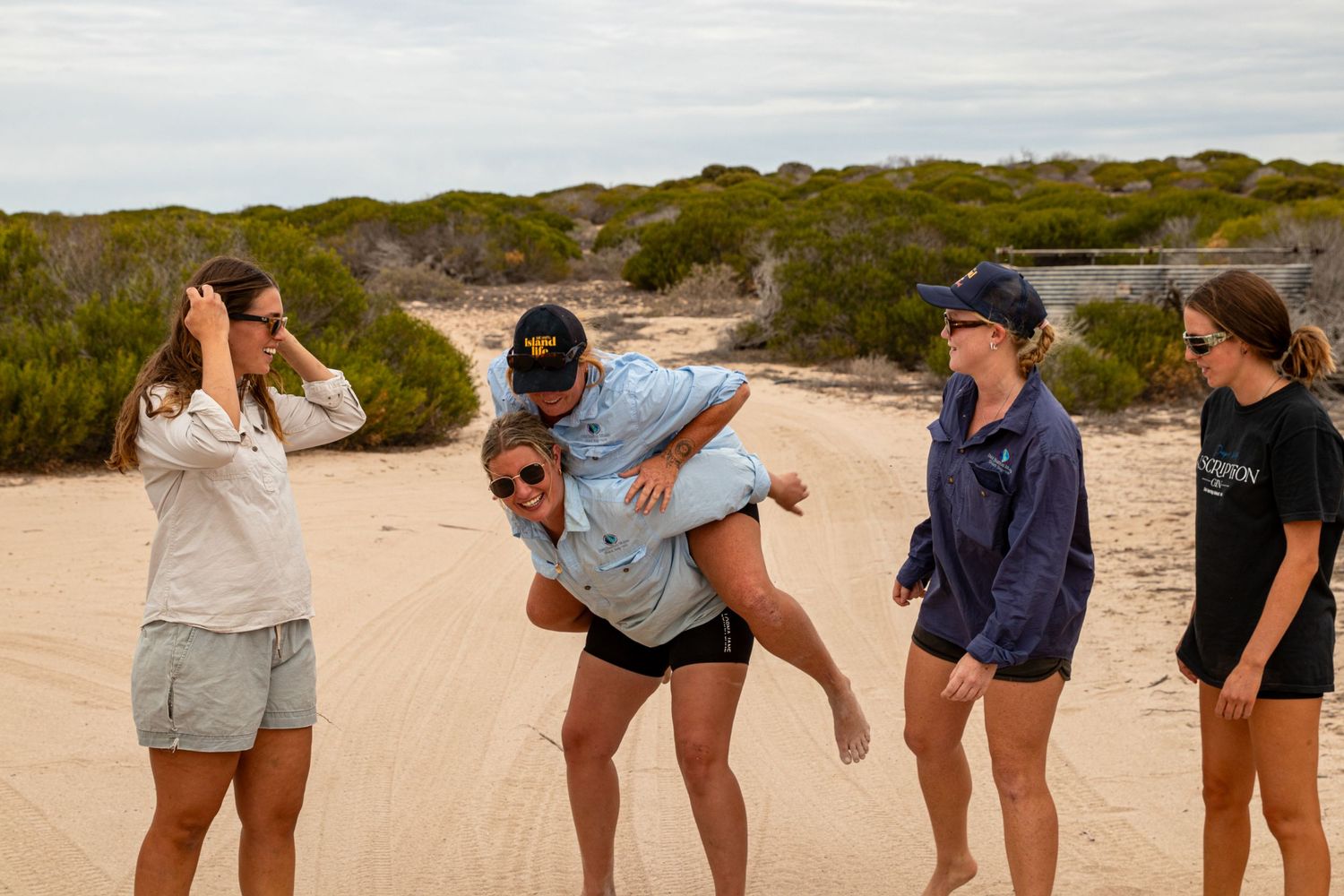 Group of women enjoying a fun piggyback ride on sandy beach dunes at Dirk Hartog Island, Western Australia.
