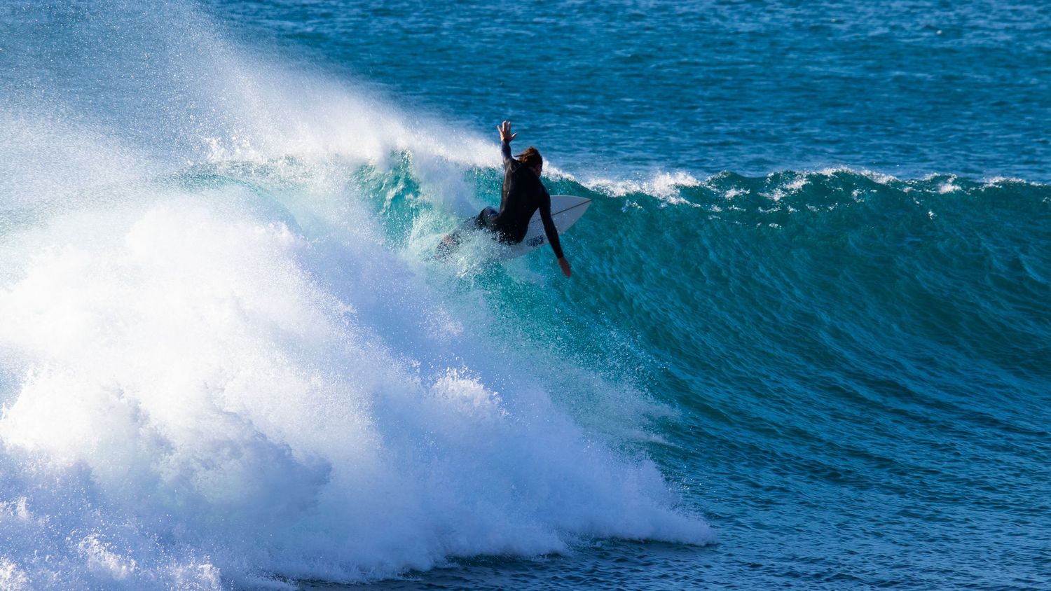 Surfer in black wetsuit performing an aerial maneuver off the top of a crashing ocean wave.