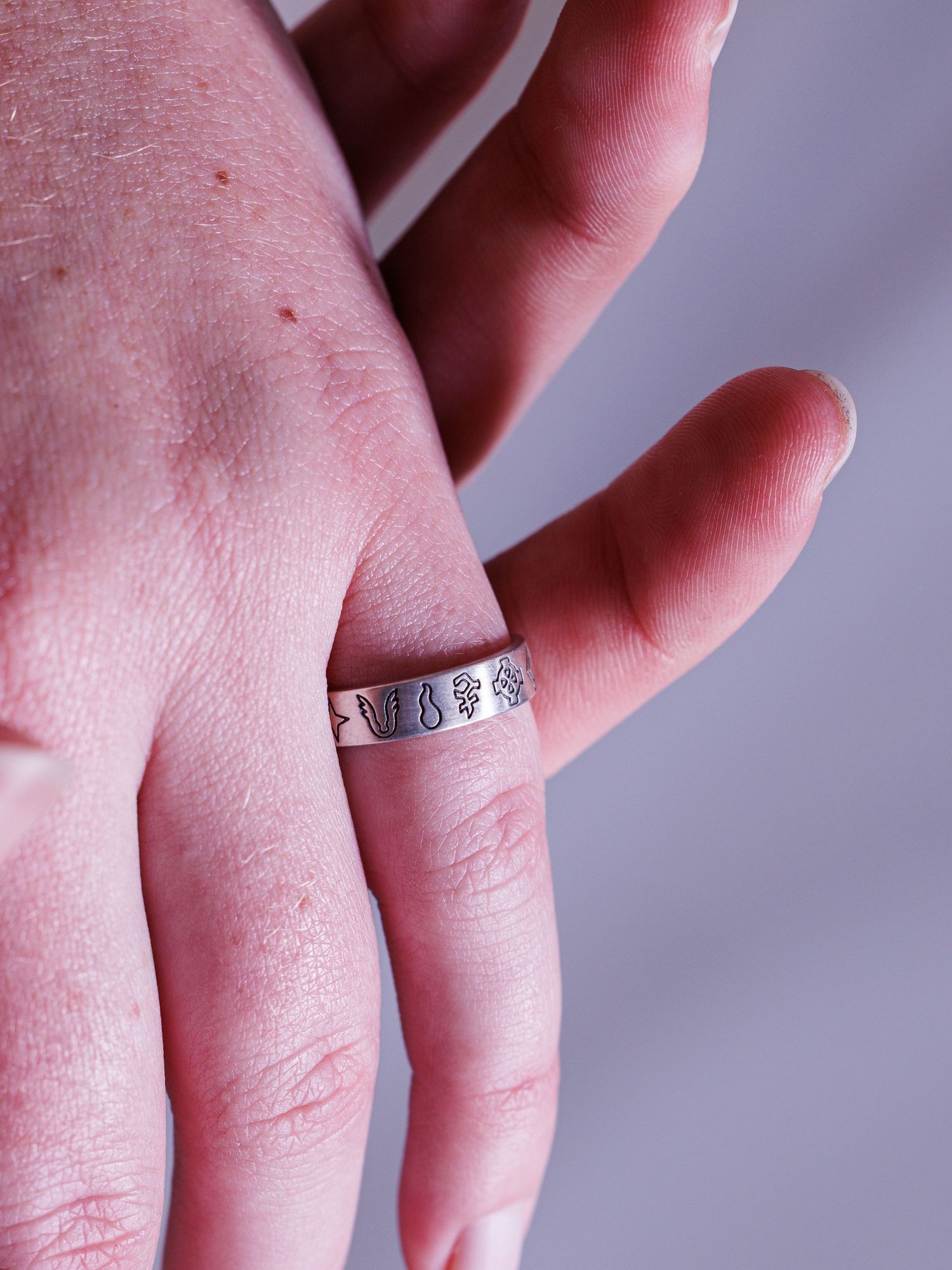 Sterling silver band ring featuring engraved symbols worn on finger, shown from palm side.