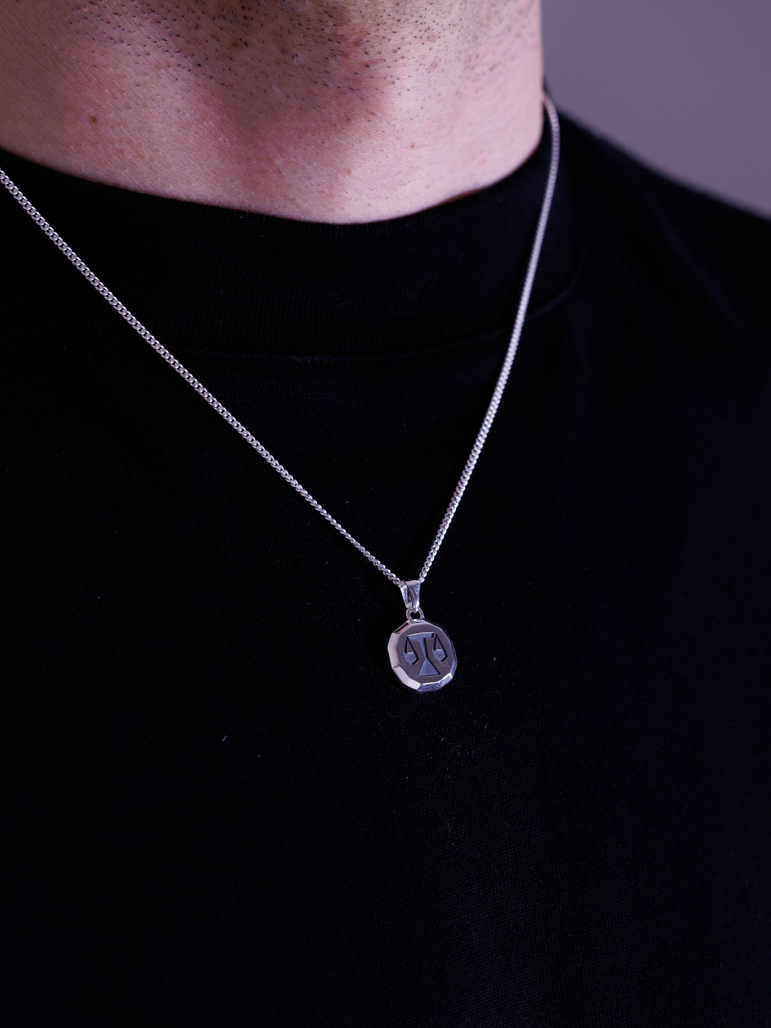 Man wearing silver round pendant with engraved symbol on box chain necklace.