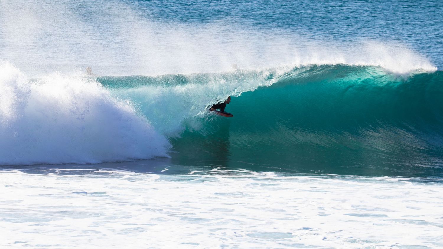 Surfer carving through a large turquoise barrel wave in clear blue ocean water.