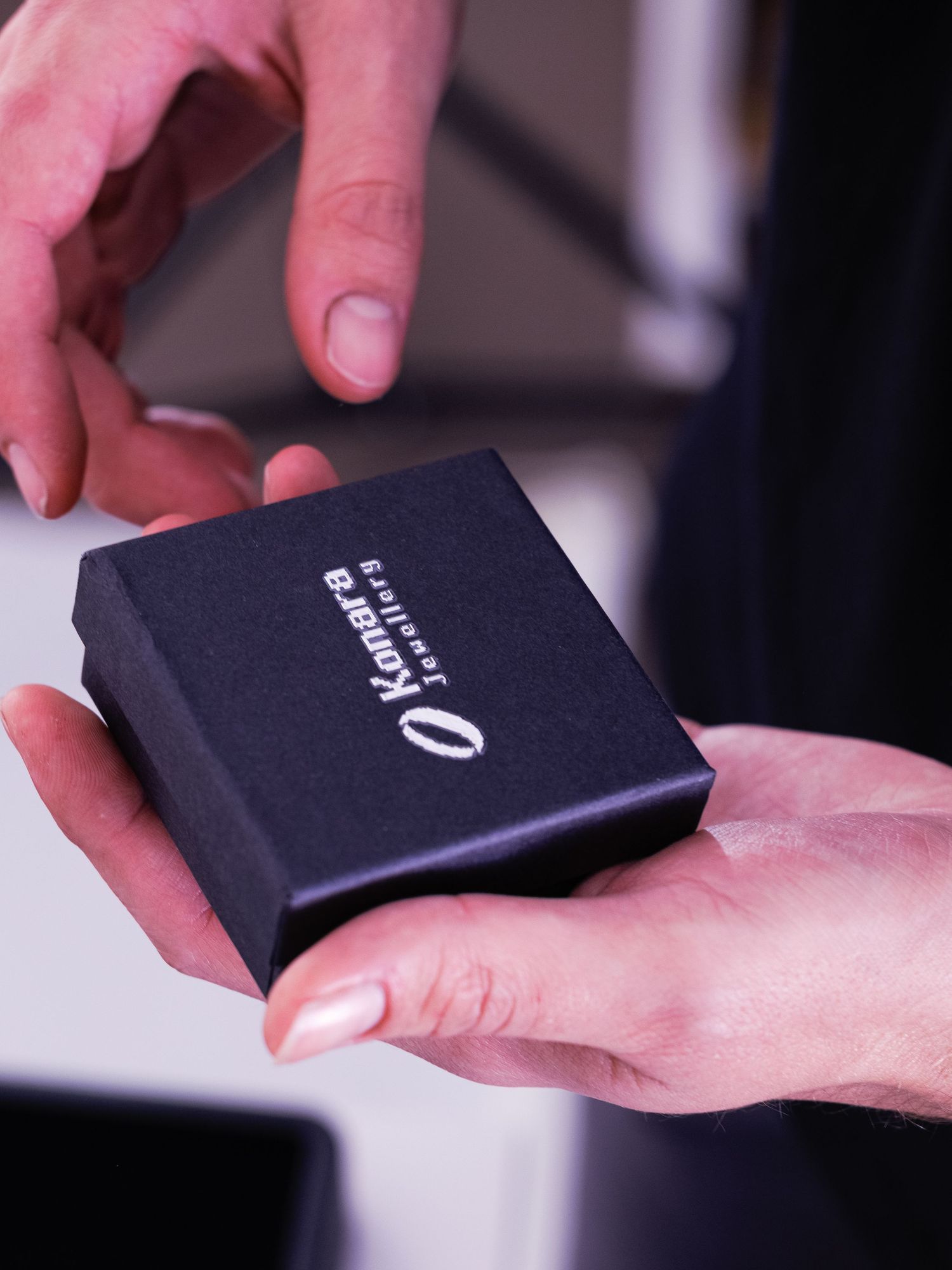 Hands holding a closed black Konara Jewellery gift box with silver logo text.