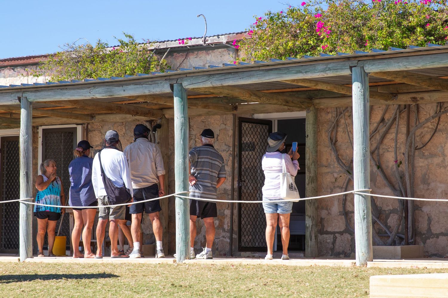 Tourists exploring a historic colonial stone building with verandah and bougainvillea in outback Australia.