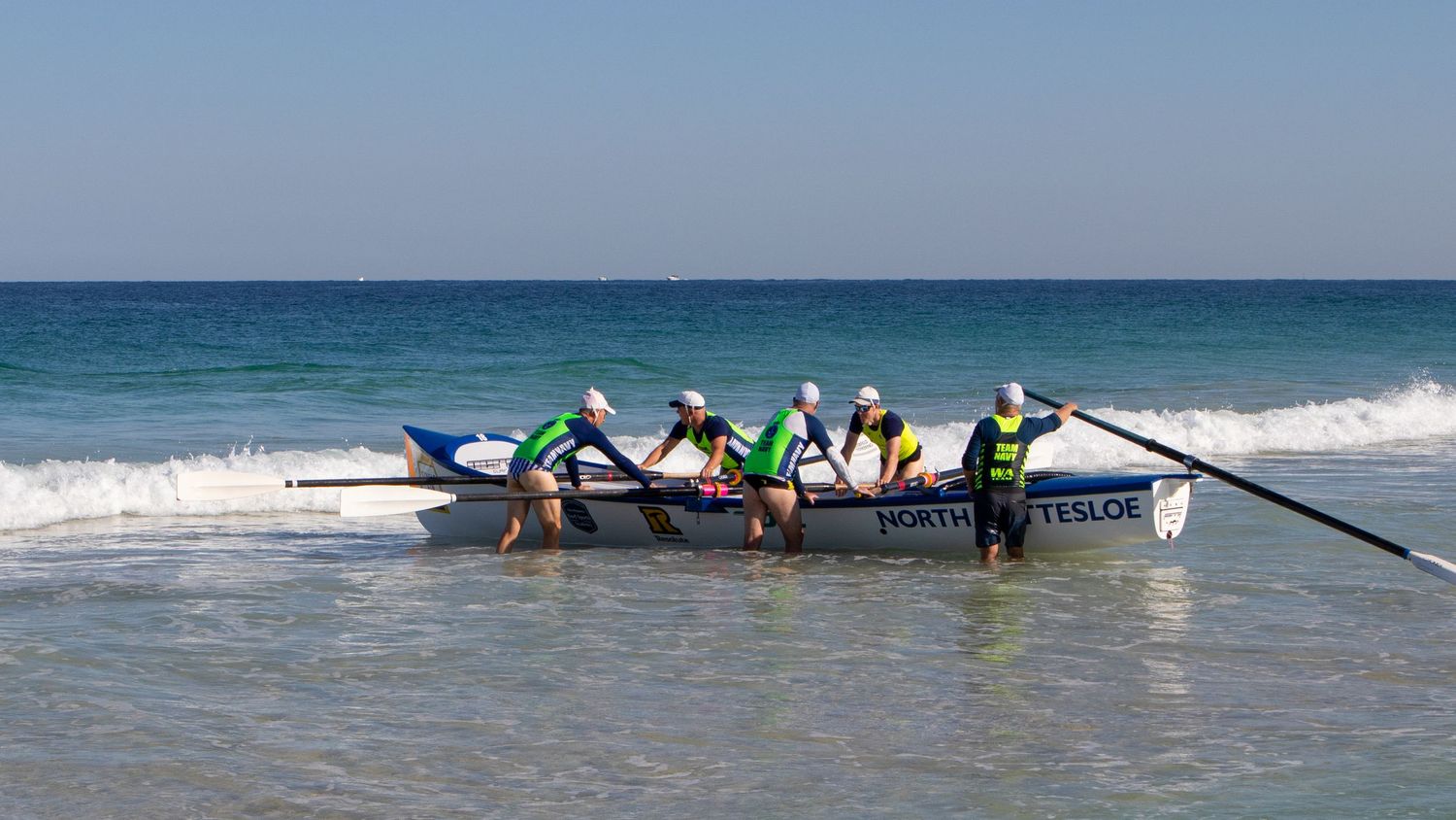 North Cottesloe surf lifesaving team rowing an outrigger canoe through ocean waves.
