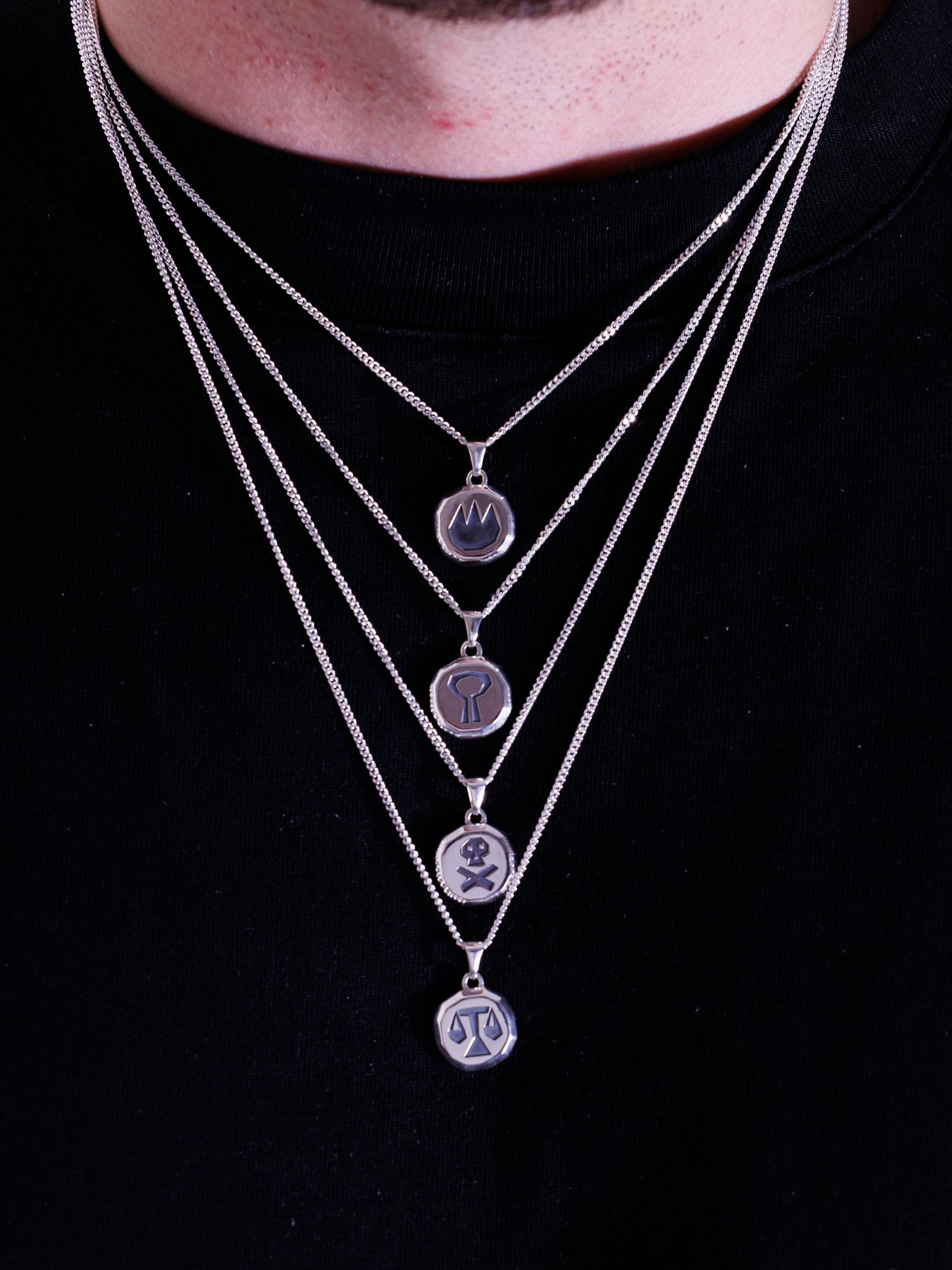 Man wearing four layered silver coin pendant necklaces with engraved symbols on a black shirt.