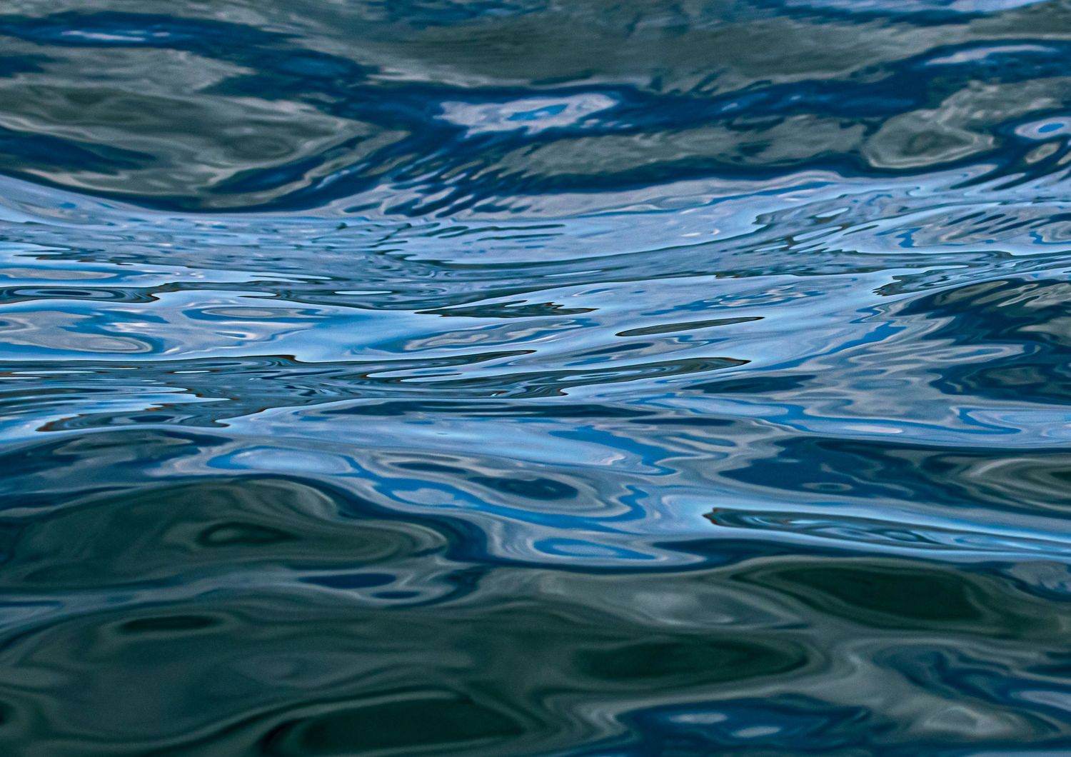 Smooth blue ocean water surface with gentle ripples showing swirling teal and blue reflections.