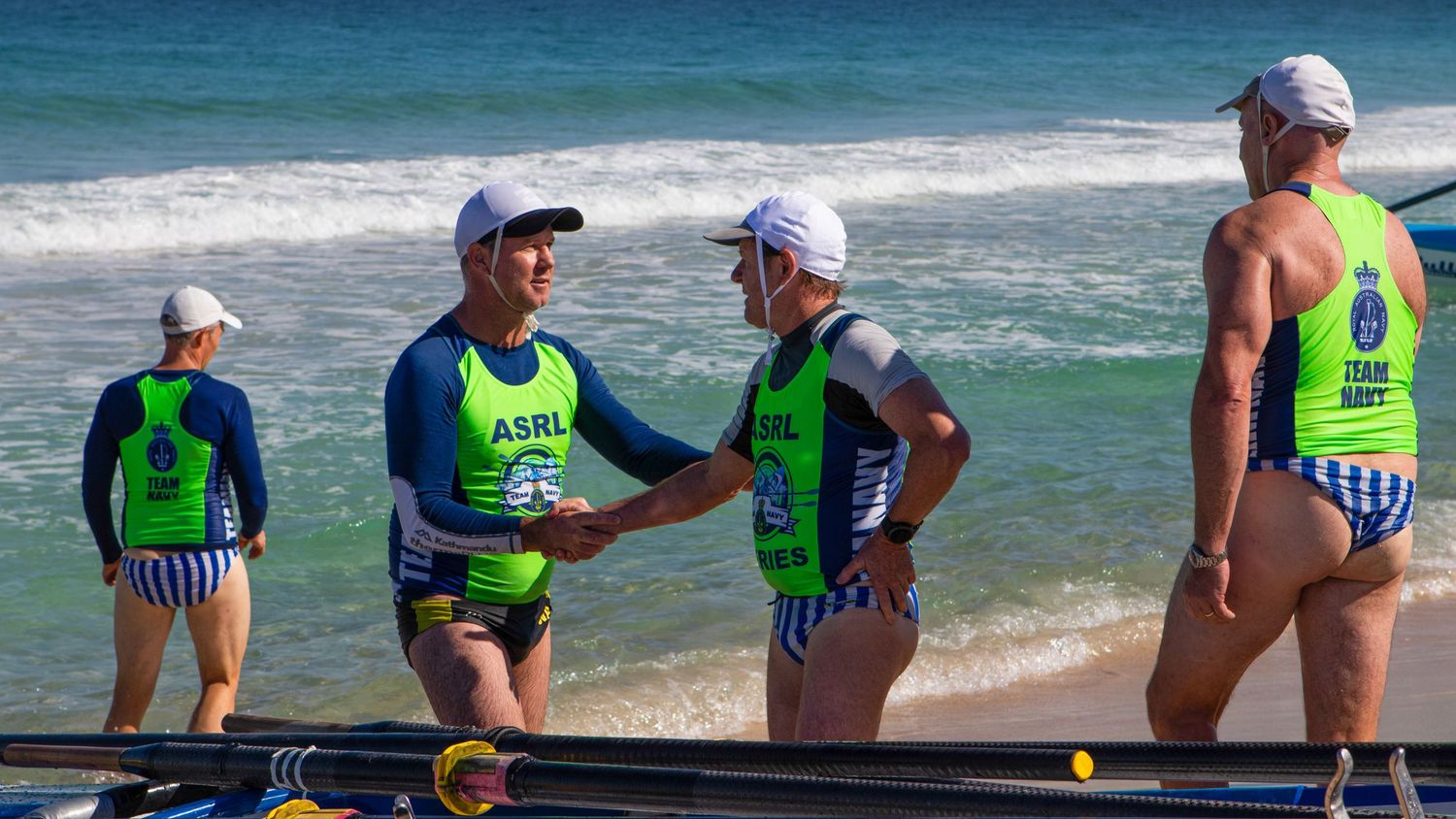 Surf boat rowing team members shake hands on a sunny beach during an ASRL Series competition.
