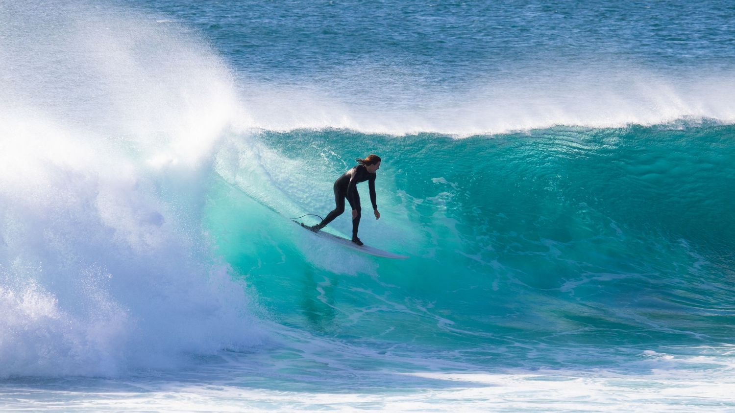 A surfer in a wetsuit rides deep inside a large curling turquoise wave on the ocean.