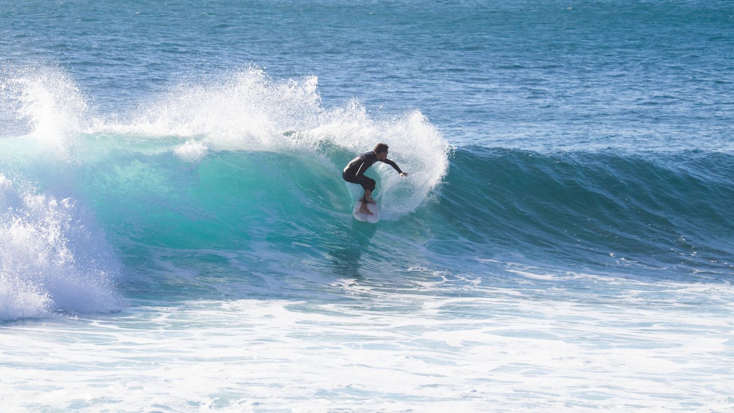 A surfer in a black wetsuit rides deep inside a powerful turquoise barreling wave.