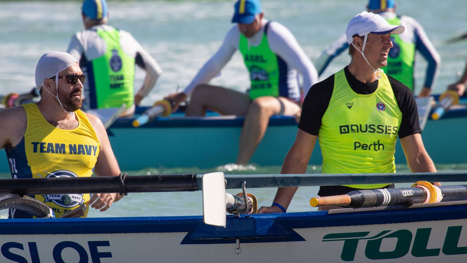 Two surf boat rowers in ASRL Series bibs compete during a beach rowing race in Perth, Australia.
