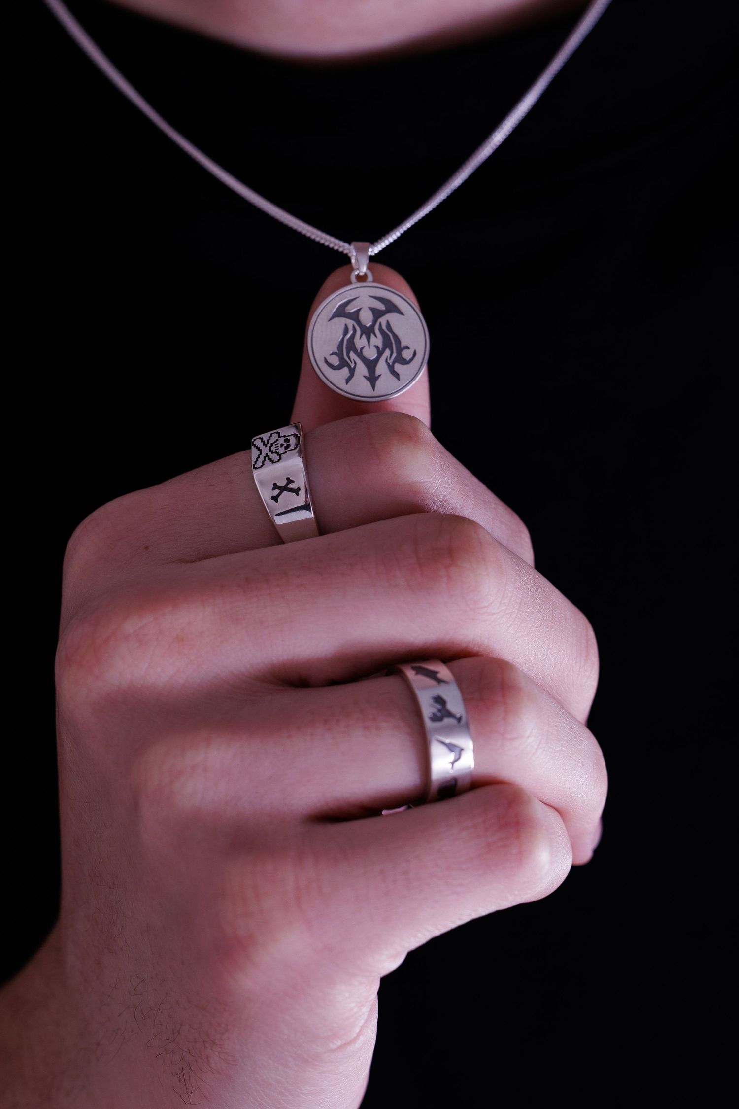 Hand holding a silver oval pendant necklace while wearing two engraved silver band rings.