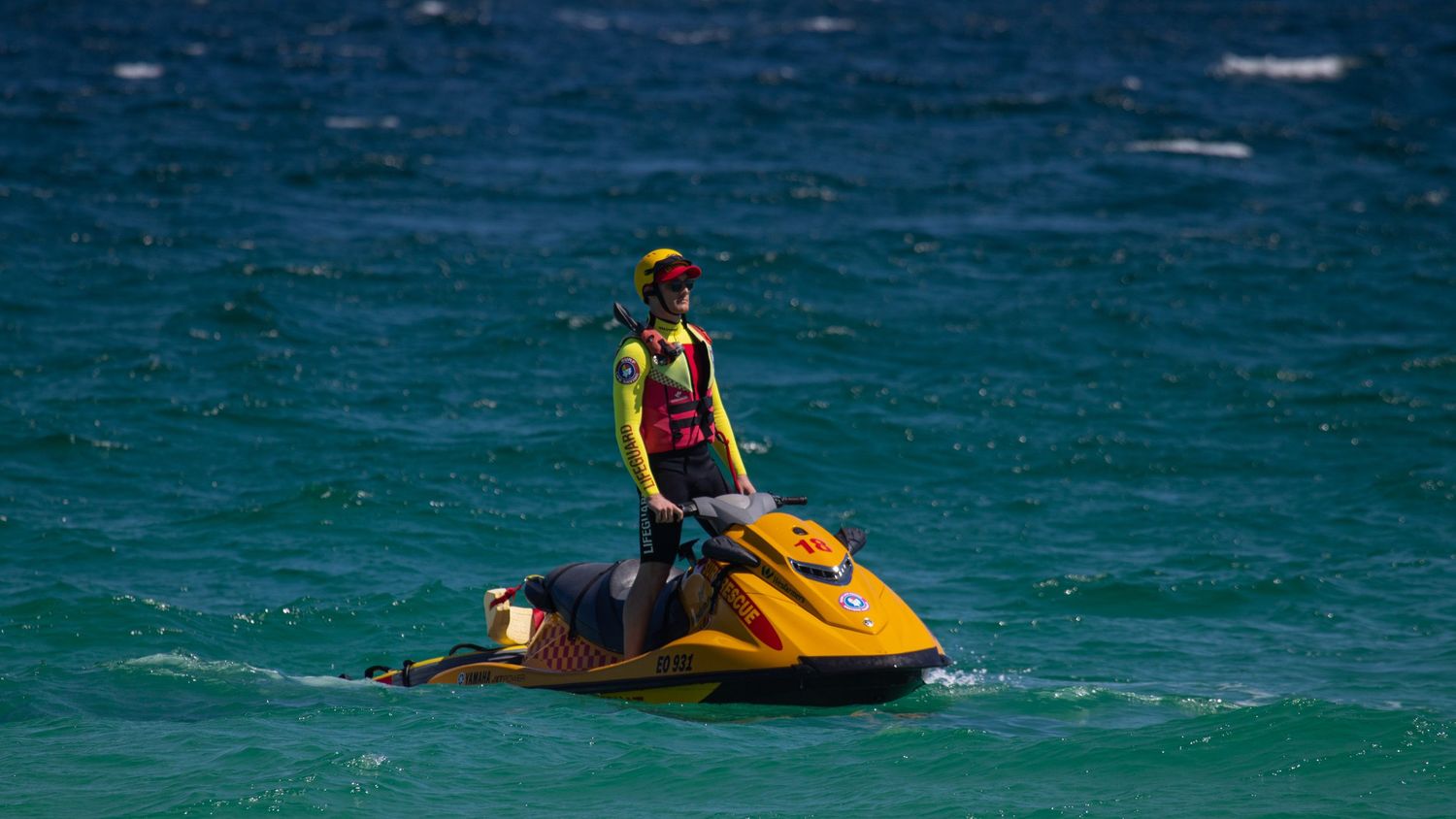 Surf lifesaving patrol officer on yellow jet ski monitoring ocean waters during beach event.