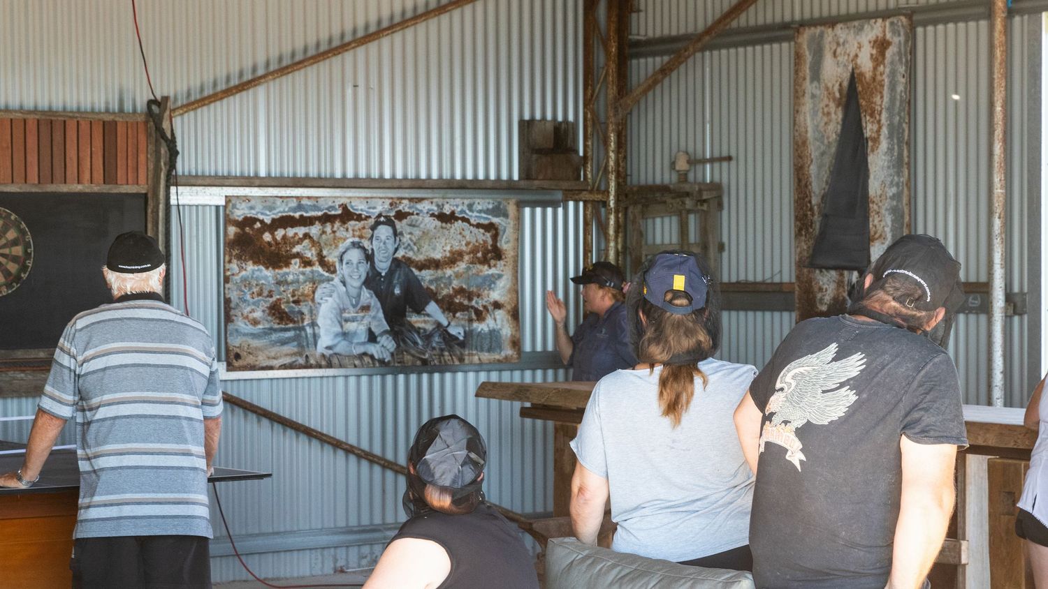 Visitors viewing maritime artwork display inside rustic corrugated iron heritage building interior.