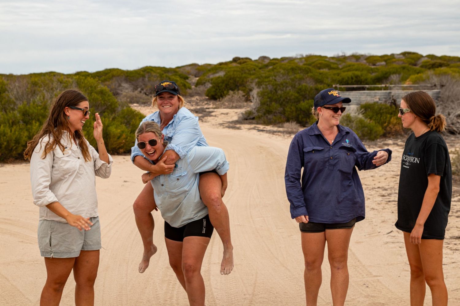 Five women laughing and playing on sandy beach trail surrounded by coastal scrubland at Dirk Hartog Island.