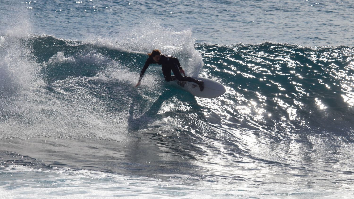 Surfer in a wetsuit riding a powerful wave on a surfboard in clear blue ocean waters.