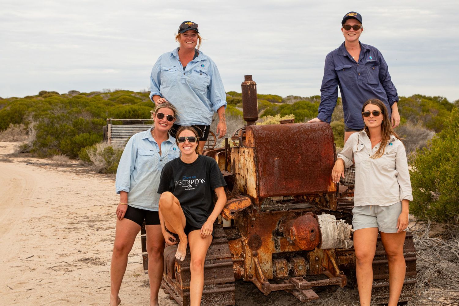 Group of five people posing with a rusty vintage bulldozer on a sandy track at Dirk Hartog Island.