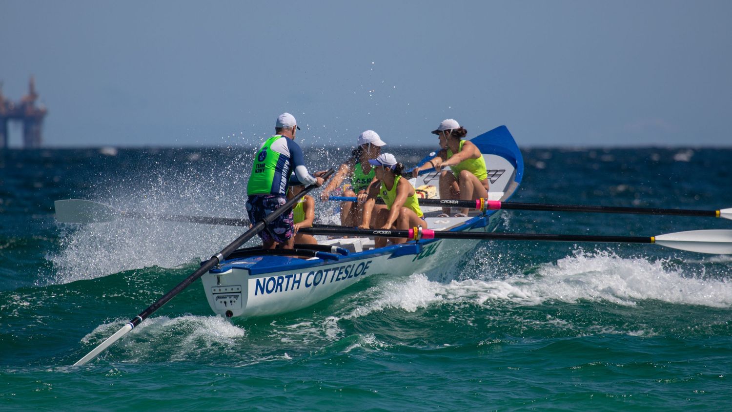 North Cottesloe surf boat crew rowing through rough ocean waves during a competitive surf lifesaving race.